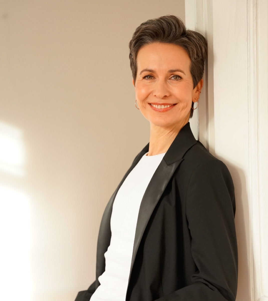 Shila Driesch lächelt in die Kamera, an eine weiße Tür gelehnt