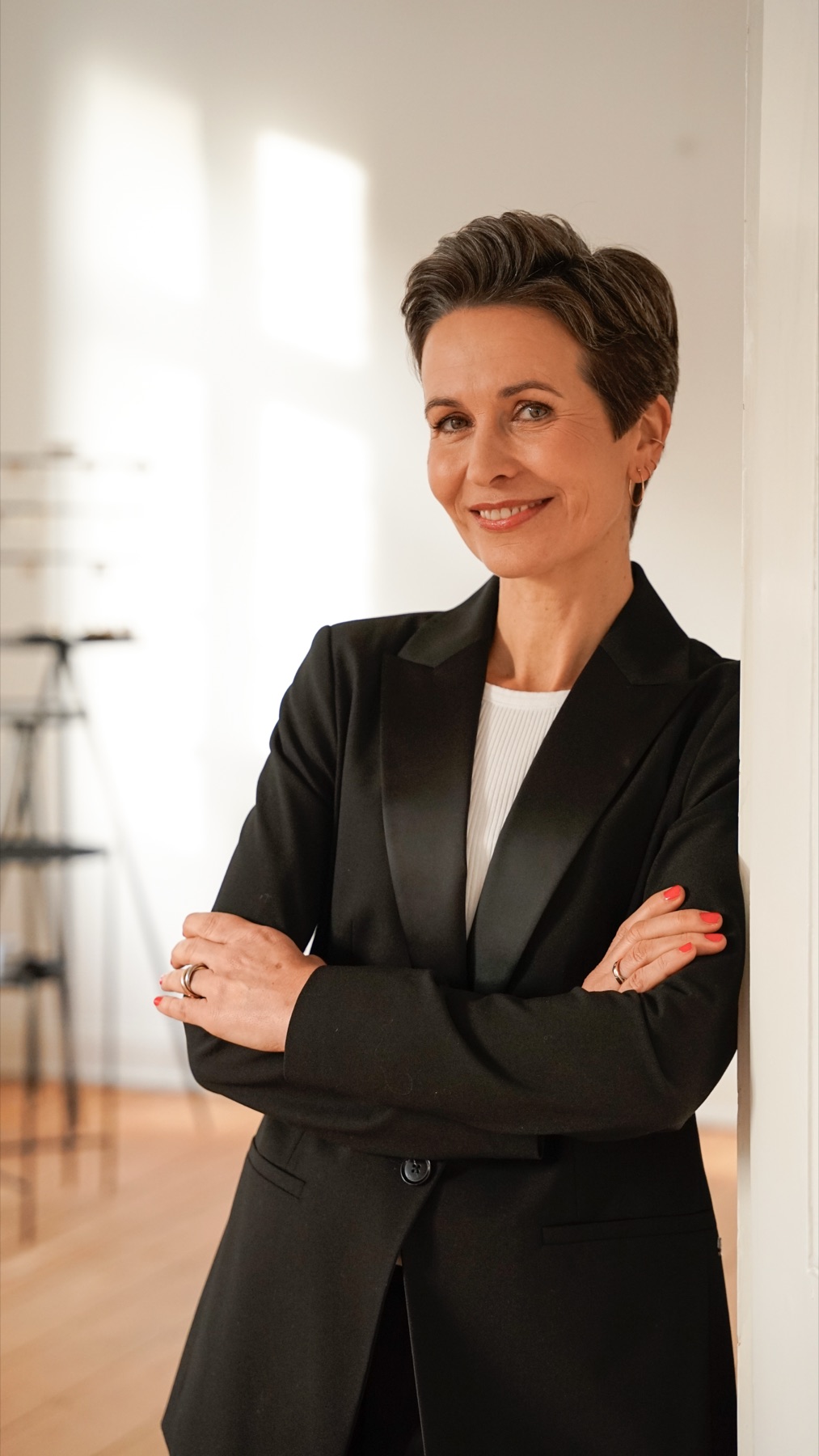 Shila Driesch, lehnt mit verschränkten Armen an einer weißen Tür und lächelt
