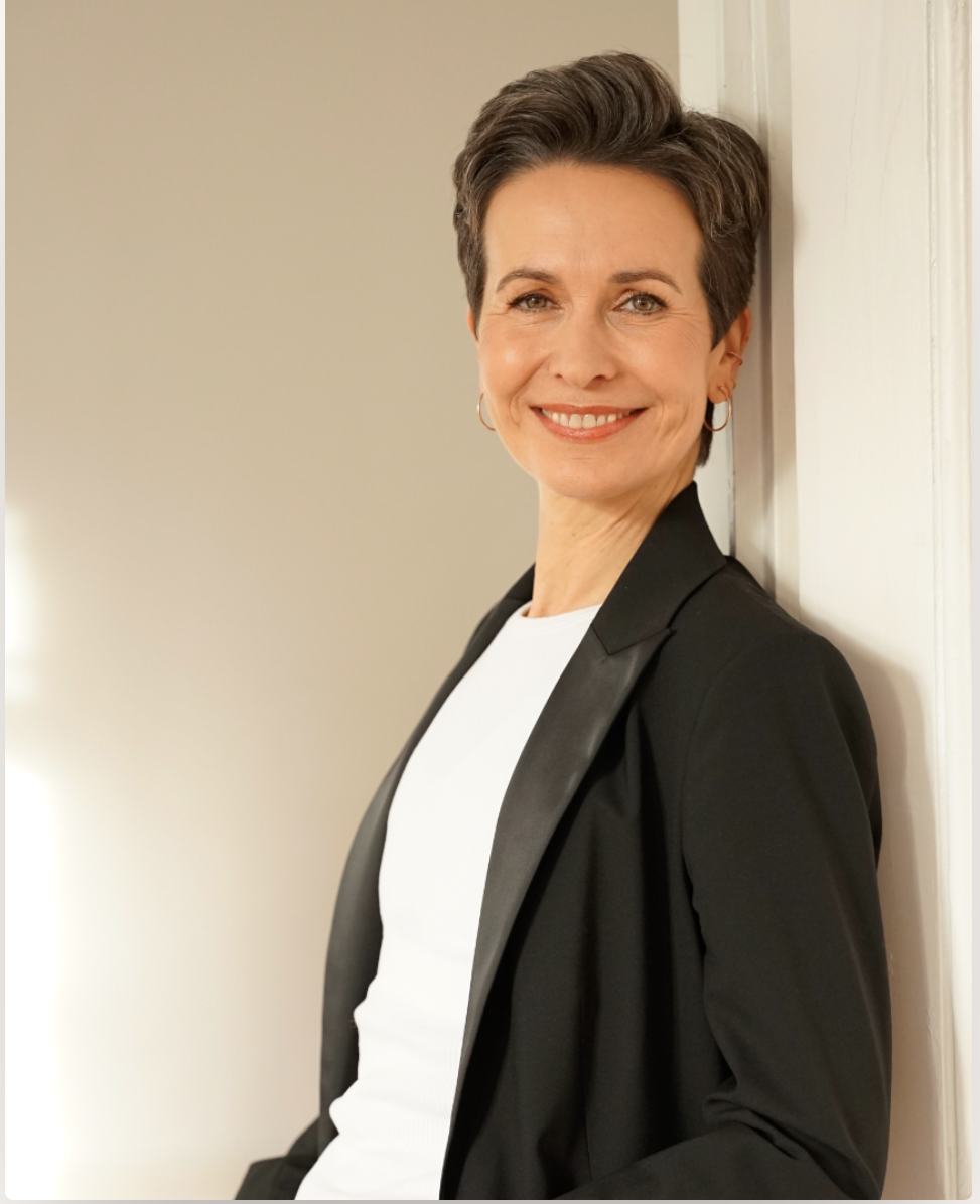 Shila Driesch im schwarzen Blazer, an eine helle Wand gelehnt